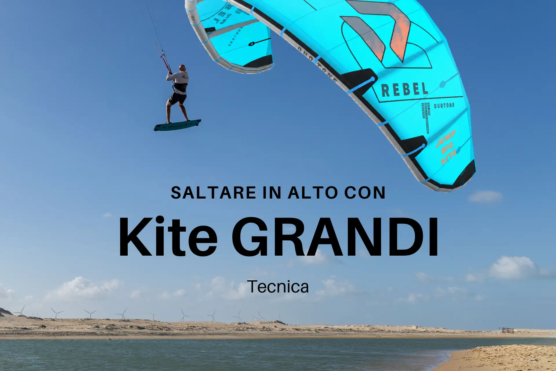 Kitesurf Big Air: atleta salta in alto con un kite grande Duotone Rebel azzurro in uno spot con acqua piatta, dune di sabbia e pale eoliche sullo sfondo