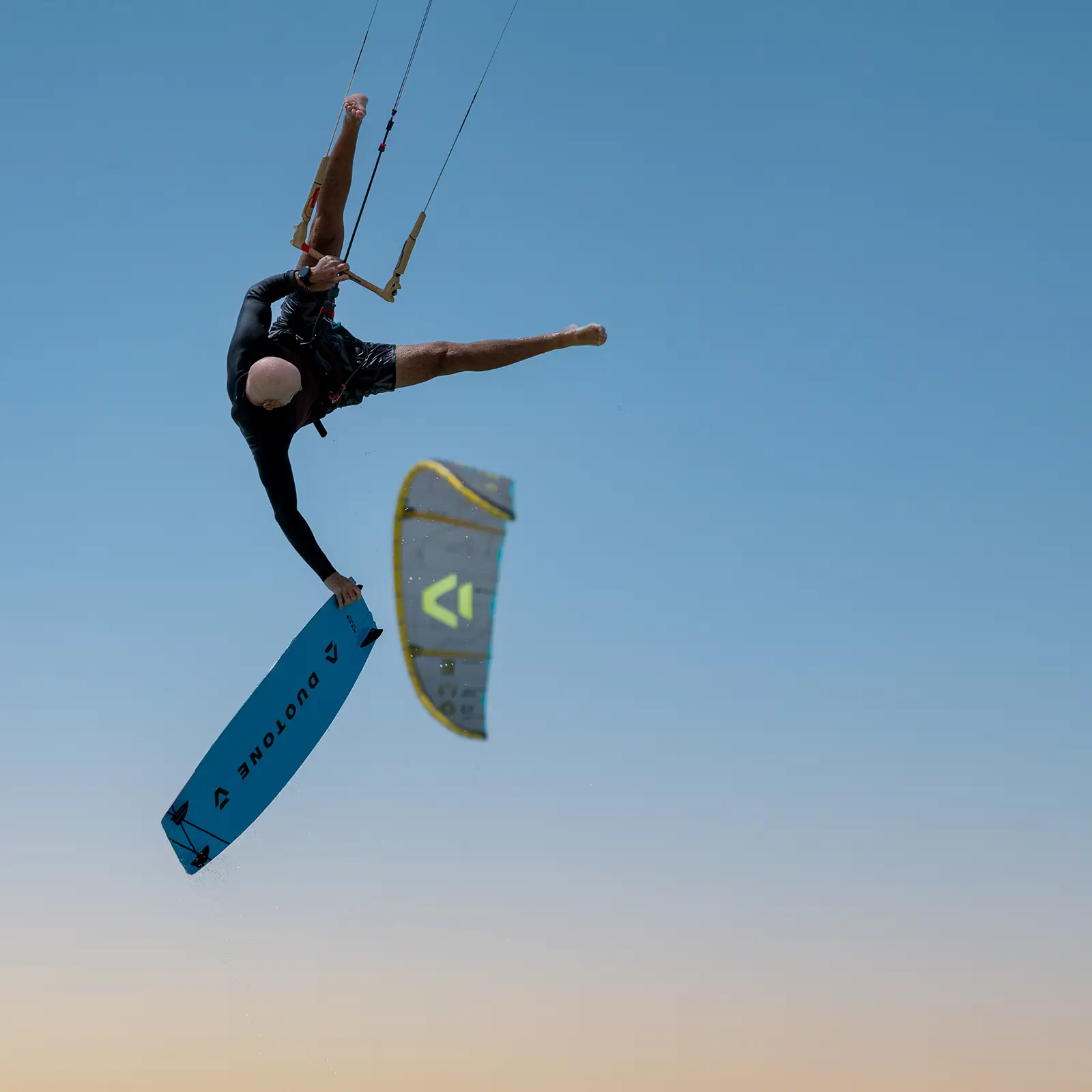 Kiter in salto con presa della tavola Duotone e kite in volo sullo sfondo, esempio di misura del kite adatta al vento